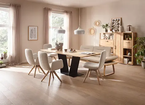 Essbereich mit Holztisch, gepolsterten Stühlen und Bank, Sideboard und Regal rechts, große Fenster mit Vorhängen links